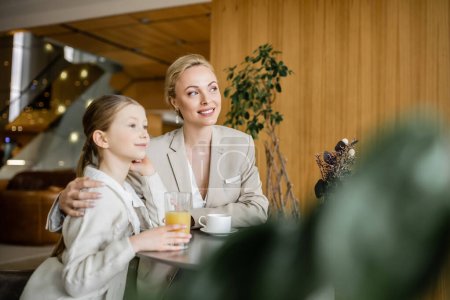 Mutter und Tochter verbringen viel Zeit miteinander, verträumte Blondine spricht mit Frühchen und hält Tasse Kaffee, arbeitende Eltern und Kind, moderne Elternschaft, familiäre Bindung 