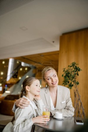 happy mother and daughter spending quality time, blonde woman hugging preteen girl and looking away near beverages and smartphone, working parent and kid, modern parenting, family bonding 