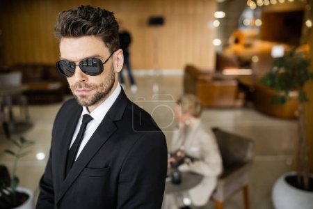 private security service, personal safety concept, handsome bodyguard in formal wear and sunglasses protecting safety of female client on blurred background, mother and daughter in cafe 