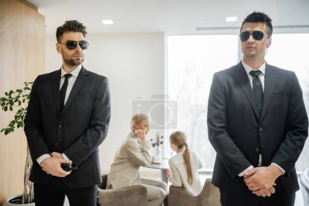 private security service, personal safety concept, good looking bodyguards in formal wear and sunglasses protecting safety of clients on blurred background, mother and daughter in cafe 