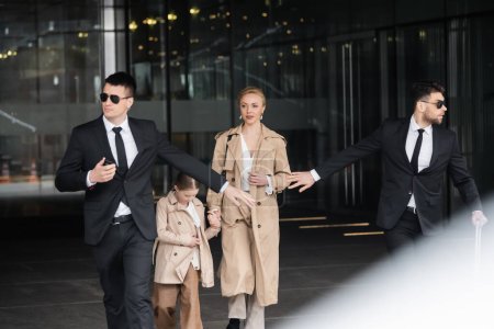 private security, personal bodyguards protecting female clients, blonde woman and daughter walking out of hotel, safety of rich family, men in formal wear and sunglasses doing their job 