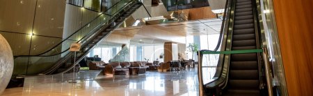 modern hotel interior with sophisticated lobby design, escalators, moving staircase, leather couches, lavish ambience, spacious and comfort, classy and chic, aesthetic, banner