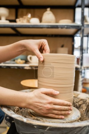 Cropped view of hands of craftswoman making clay vase on pottery wheel in workshop