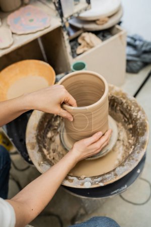 Vista de ángulo alto de la mujer artesana haciendo jarrón de arcilla en la rueda de cerámica en taller de cerámica