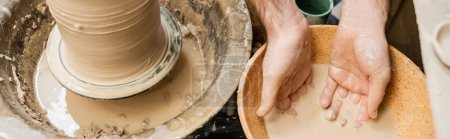 Téléchargez les photos : Vue du dessus de l'artisan travaillant avec de l'eau dans un bol près de l'argile et de la roue de poterie dans un studio en céramique, bannière - en image libre de droit