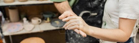 Photo for Cropped view of couple of potters in aprons holding hands while working in ceramic workshop, banner - Royalty Free Image
