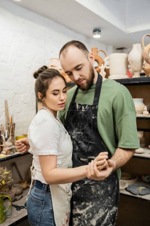 Couple de sculpteurs dans des tabliers tenant la main tout en travaillant ensemble dans un atelier de poterie