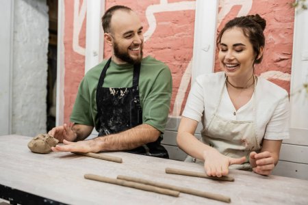 Fröhliches Bildhauerpaar in Schürzen modelliert Ton und spricht in Keramikwerkstatt