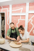 Couple of sculptors shaping clay bowl while working together in ceramic workshop Poster #665332592