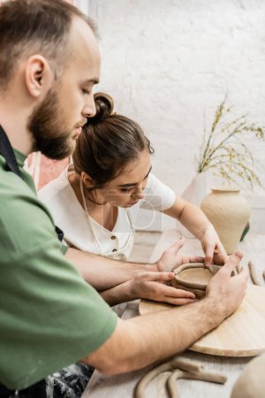Foto de Artesana en delantal formando tazón de barro con novio juntos en taller de cerámica - Imagen libre de derechos