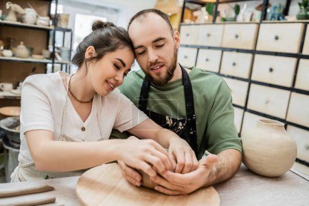 Photo for Positive romantic couple of potters making clay bowl in ceramic workshop at background - Royalty Free Image