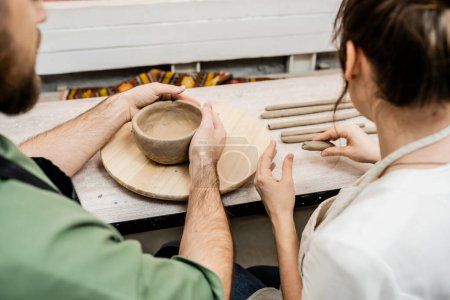 Téléchargez les photos : Vue recadrée de l'artisan en tablier façonnant bol d'argile près de petite amie dans l'atelier de poterie - en image libre de droit