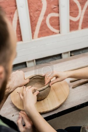 Photo for Blurred couple of potters creating clay bowl and working in ceramic workshop at background - Royalty Free Image
