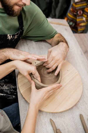 High angle view of couple of potters shaping clay bowl on wooden board in workshop
