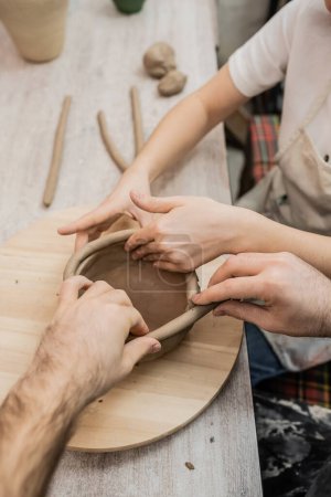 Cropped view of craftswoman creating clay bowl with boyfriend together in pottery workshop