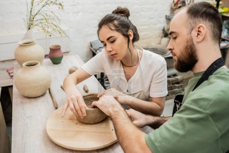 Töpferpaar in Schürzen formt Tonschale, während es in der Keramikwerkstatt in der Nähe von Vasen auf dem Tisch arbeitet