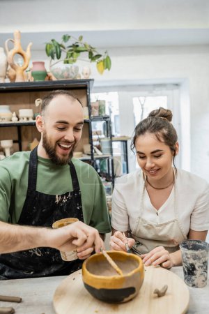 Positivo pareja romántica de artesanos para colorear utensilios de cocina de arcilla juntos en taller de cerámica