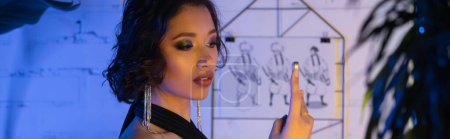 Trendige Asiatin im Kleid macht Selfie mit Smartphone in Nachtclub mit Neonlicht, Banner