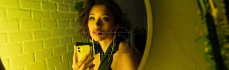 Photo for Trendy asian woman taking selfie on smartphone near mirror in neon light and night club, banner - Royalty Free Image