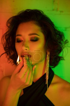 Portrait of stylish asian woman holding match with fire while standing in night club with neon light