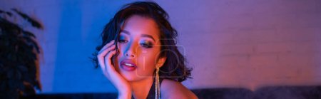 Trendy junge asiatische Frau mit Make-up und Frisur steht im Neonlicht in Nachtclub, Banner