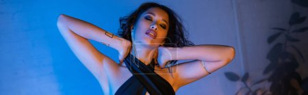 Sexy young asian woman touching neck while standing in night club with neon light, banner