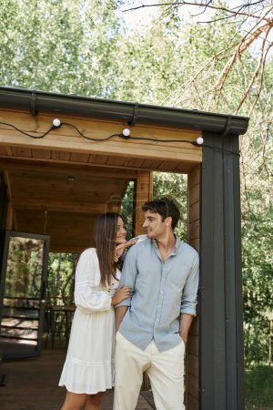 man and beautiful woman in sundress standing near vacation house, love and romance, happy couple