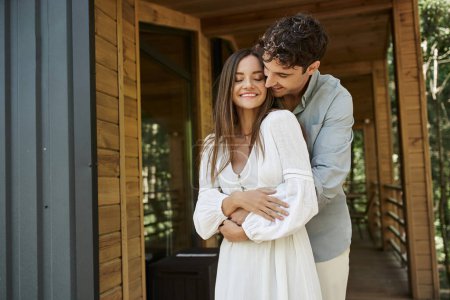 Foto de Feliz hombre abrazando novia en vestido blanco cerca de la casa de vacaciones, verano, escapada romántica - Imagen libre de derechos