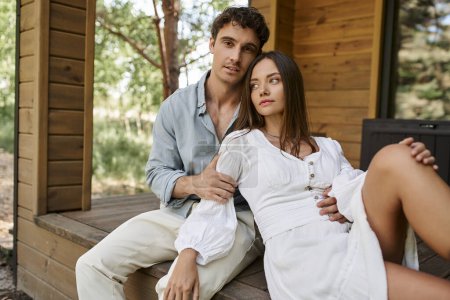 Romantischer Kurzurlaub, Mann umarmt glückliche Frau in Sundress, während er auf der Veranda des Ferienhauses sitzt