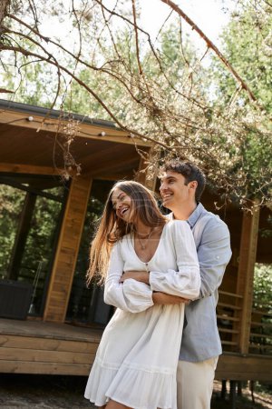 Lachen, glücklicher Mann umarmt Frau in weißer Uniform in der Nähe von Ferienhaus, Sommerliebe, Romantik