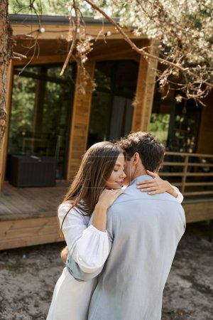 Brunette woman in sundress embracing boyfriend near blurred summer house at background outdoors