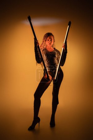 Photo for African american woman holding fluorescent lamps on yellow background, high heels and fishnet tights - Royalty Free Image