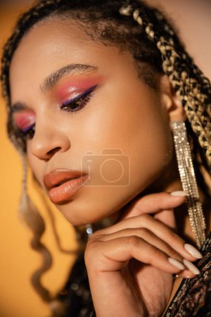 portrait of beautiful dark skinned woman posing on yellow background, bold makeup, manicure, beauty