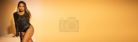 Téléchargez les photos : Bannière, afro-américaine en collants résille sexy posant sur fond jaune, regardez la caméra - en image libre de droit