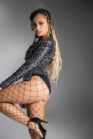 Photo for Sexy fishnet tights, bold style, african american woman on grey background, look at camera - Royalty Free Image