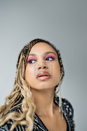 pretty african american woman with bold makeup posing on grey background, looking away, fashion