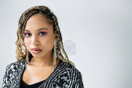 portrait of african american woman looking at camera on grey background, bold makeup, earrings