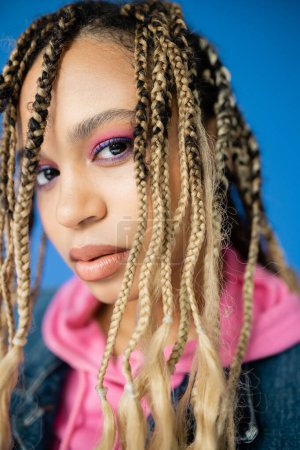 close up of african american woman with dreadlocks looking at camera on blue background, diversity