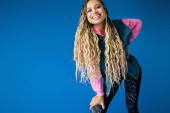 happy african american woman in pink hoodie and denim vest posing on blue background, dreadlocks puzzle #666729720