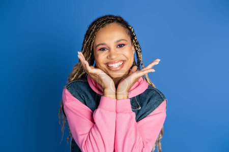 happy african american woman smiling and looking at camera on blue background, denim vest, style