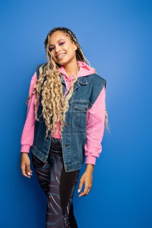 pretty woman with dreadlocks standing in leggings and pink hoodie on blue background, diversity