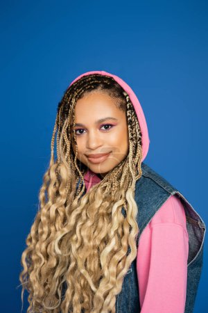 retrato de mujer afroamericana en capucha rosa sonriendo y mirando a la cámara, fondo azul