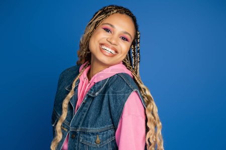 bold makeup look, happy african american woman smiling and looking at camera on blue background