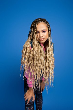 beautiful african american woman with dreadlocks and bold makeup looking at camera on blue