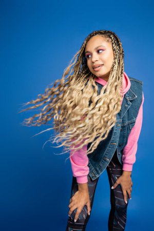 charming african american woman with dreadlocks and long hair posing on blue background in studio