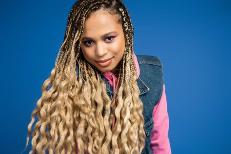 charming african american woman with dreadlocks and long hair looking at camera on blue background