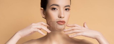 Asian woman with naked shoulders and natural makeup looking at camera isolated on beige, banner