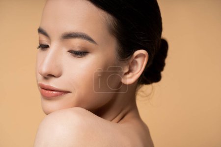 Photo for Young asian woman with naked shoulder and natural makeup posing while standing isolated on beige - Royalty Free Image