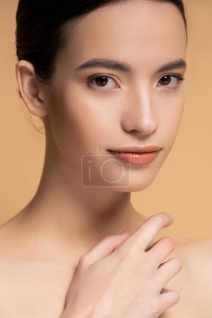 Close up view of young asian woman with naked shoulders looking at camera isolated on beige