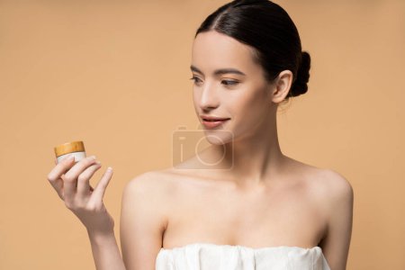 Téléchargez les photos : Positif jeune asiatique femme en haut tenant la crème cosmétique tout en se tenant isolé sur beige - en image libre de droit